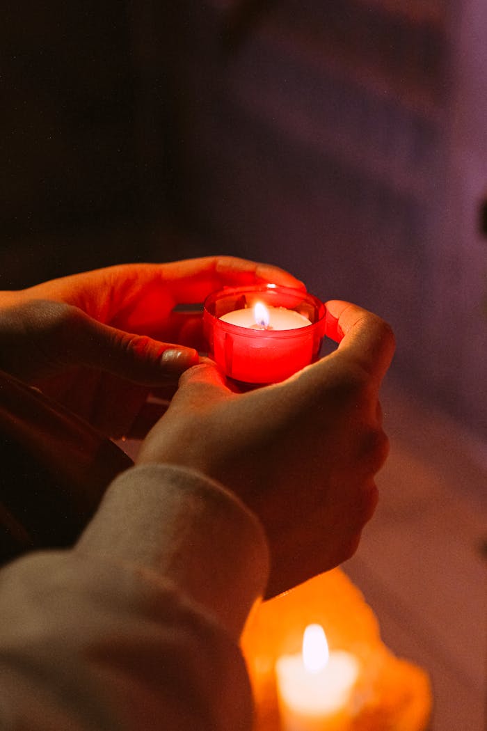 about-us Hands holding a red votive candle flame, symbolizing hope, prayer, and spirituality.